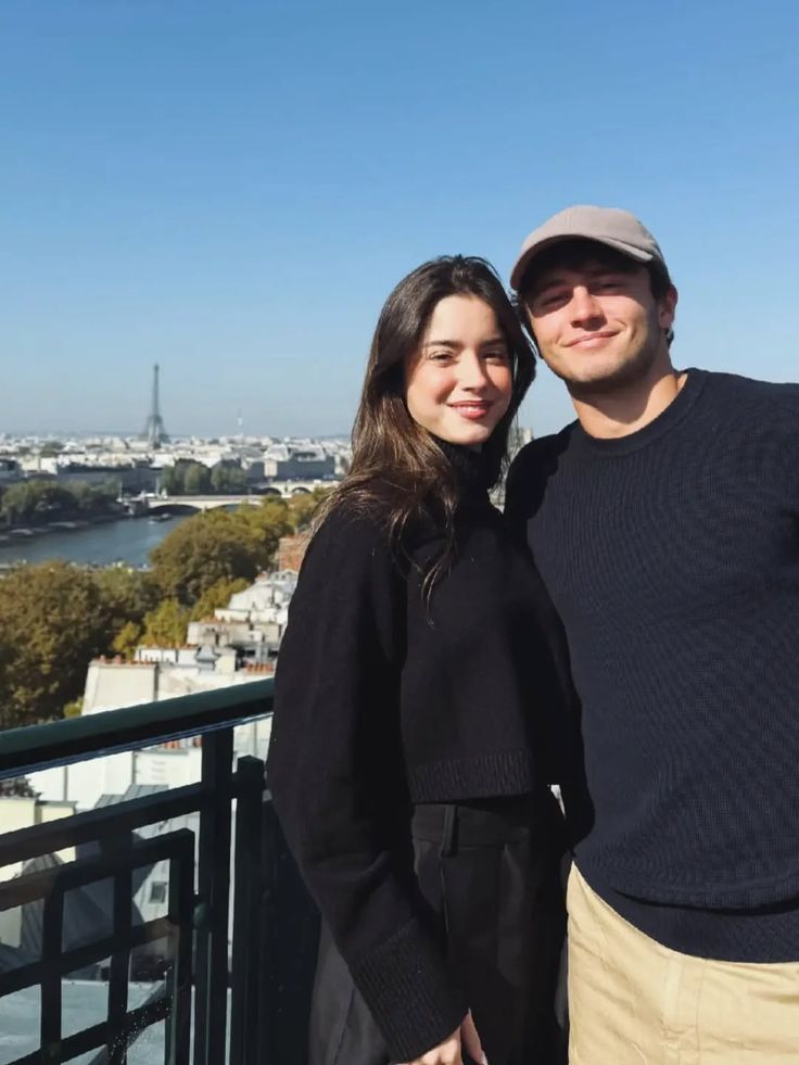 Foto asli pasangan berpakaian hitam dan biru tua dengan pemandangan Paris di belakangnya